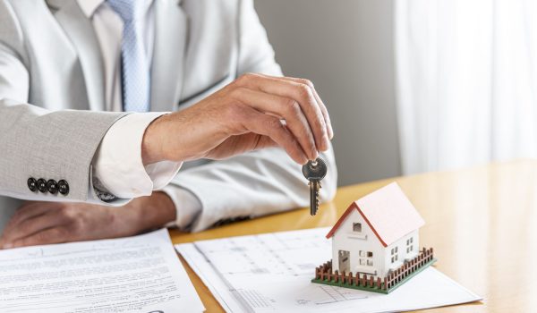 person-holding-house-keys-toy-model-house-desk (1)